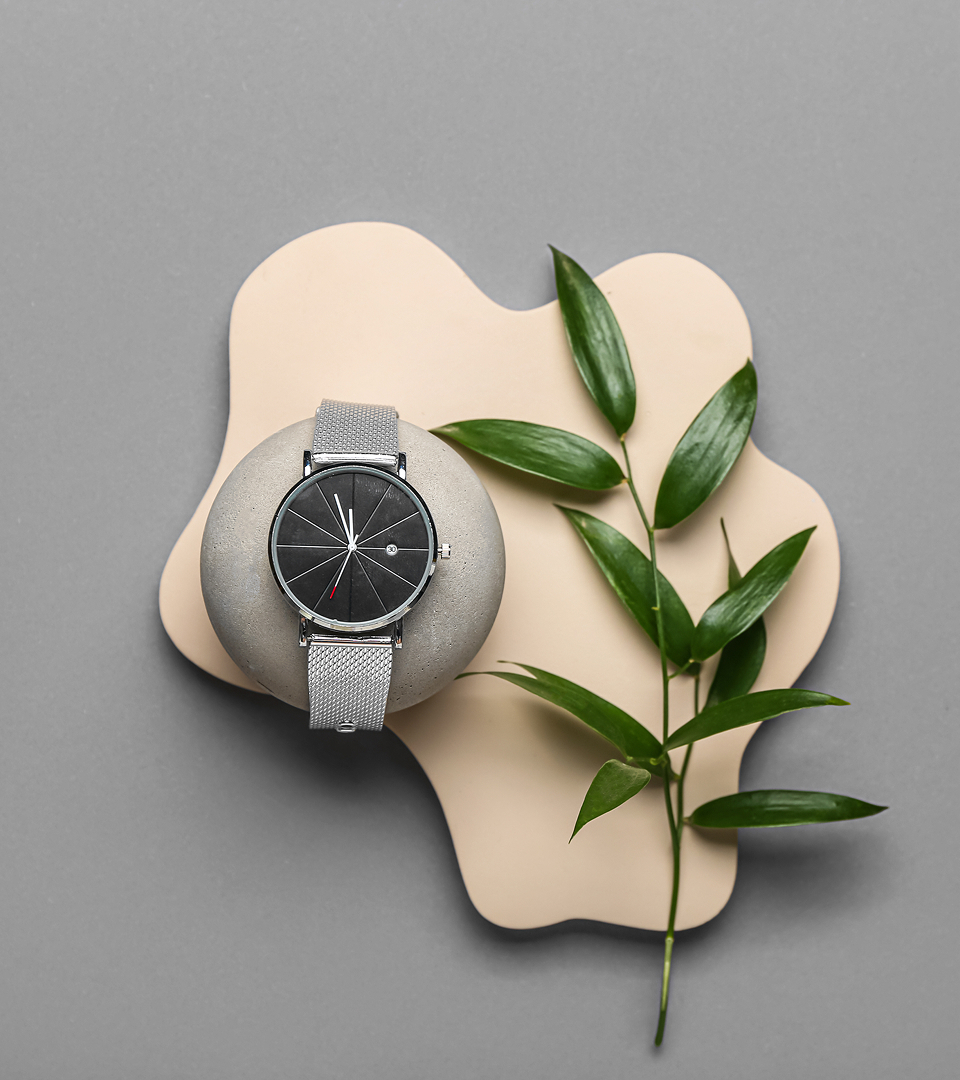 Fotografía cenital de un reloj, a la derecha una rama verde de árbol